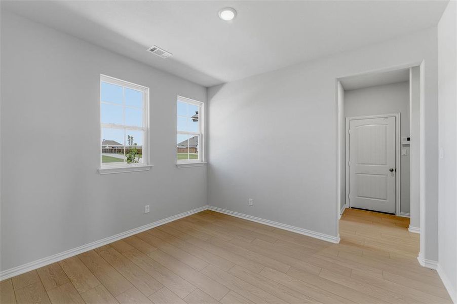 Room featuring light wood-finish flooring, light gray wall paint, and white baseboards Room featuring light wood-finish flooring, light gray wall paint, and white baseboards