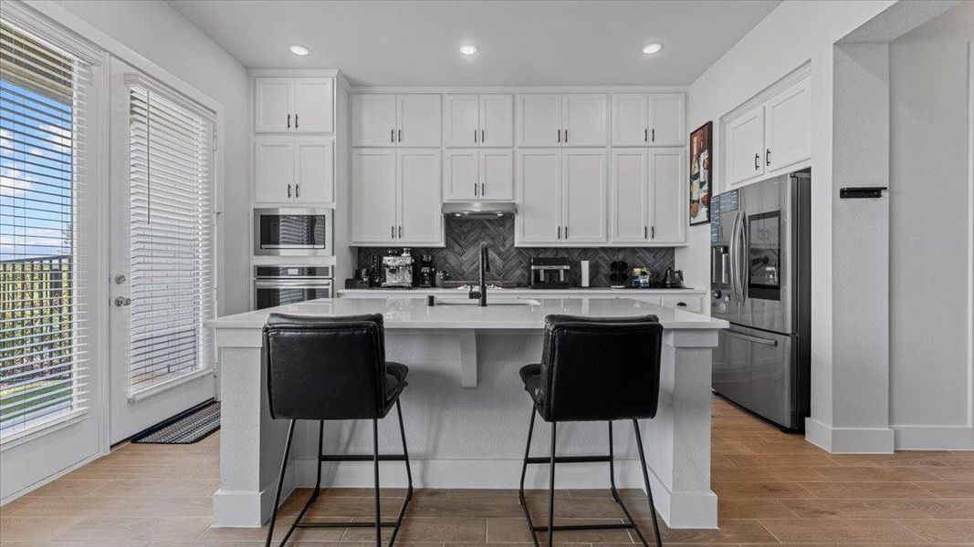 Kitchen featuring appliances with stainless steel finishes, white cabinetry, a kitchen breakfast bar, a center island with sink, and wood tiled floors Kitchen featuring appliances with stainless steel finishes, white cabinetry, a kitchen breakfast bar, a center island with sink, and wood tiled floors
