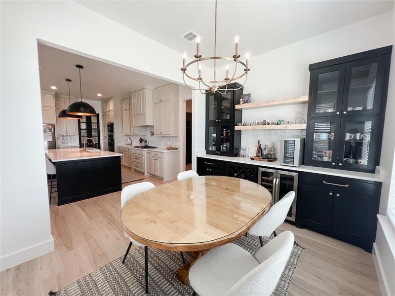 Dining room with a chandelier, light wood-type flooring, wine cooler, recessed lighting, and a bar