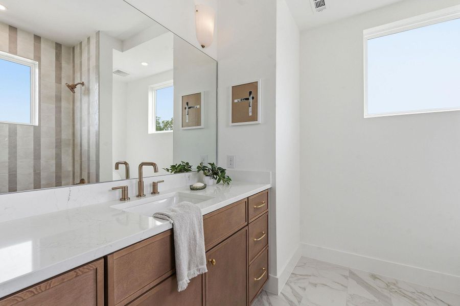 Bathroom featuring a spacious vanity with a white countertop and dual integrated sinks, wood-finish cabinetry with gold-tone hardware, a large wall-mounted mirror, and tile flooring