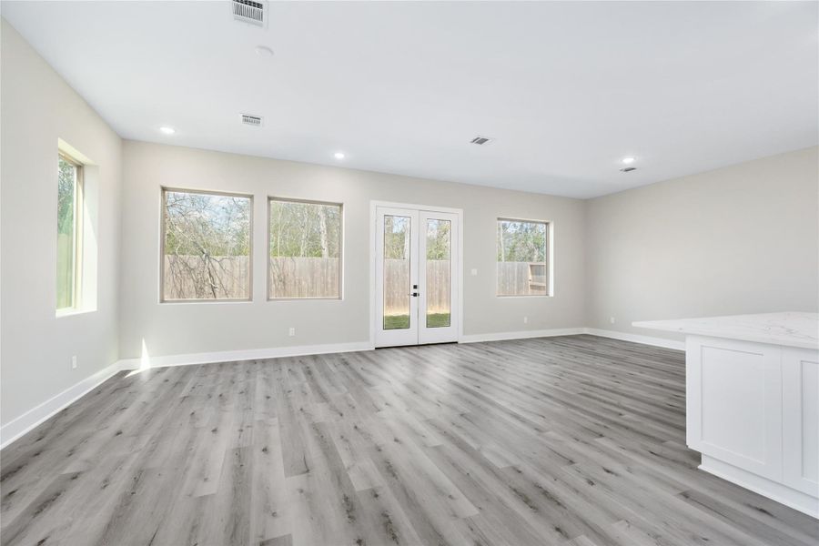 The spacious, open-concept living area features luxury vinyl plank flooring, neutral walls, and abundant natural light from large windows. French doors lead to the backyard, creating a seamless indoor-outdoor flow.