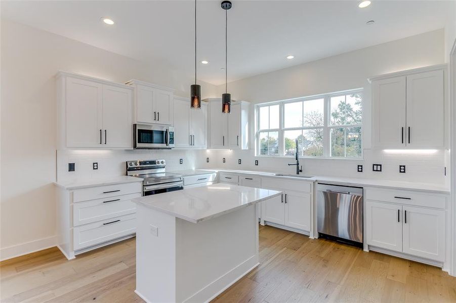 Kitchen featuring white cabinetry, light hardwood / wood-style flooring, pendant lighting, and appliances with stainless steel finishes