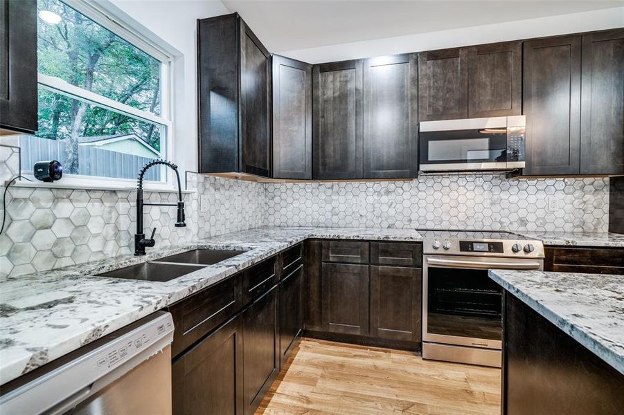 Kitchen featuring stainless steel appliances, light wood-type flooring, backsplash, light stone countertops, and sink