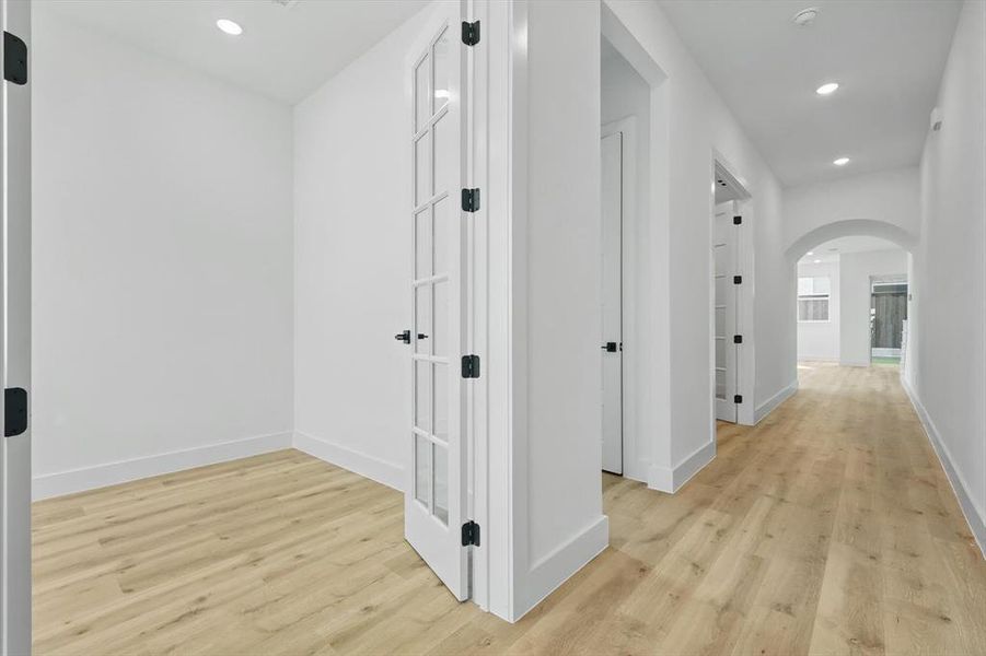 Corridor with arched walkways, light wood-style flooring, baseboards, and recessed lighting