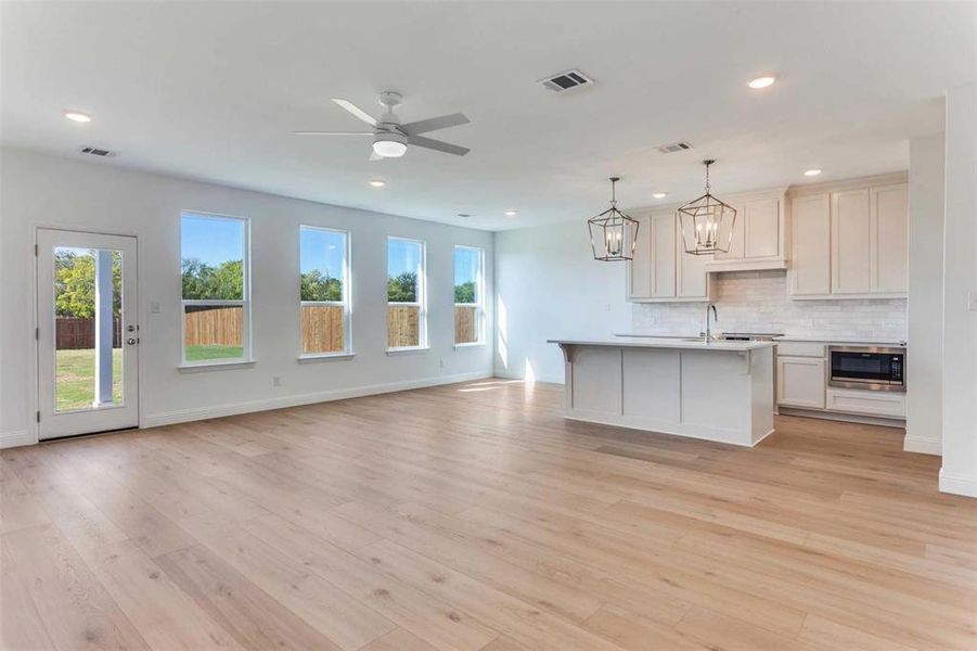 Kitchen with pendant lighting, decorative backsplash, light wood-style flooring, a kitchen island with sink, and open floor plan