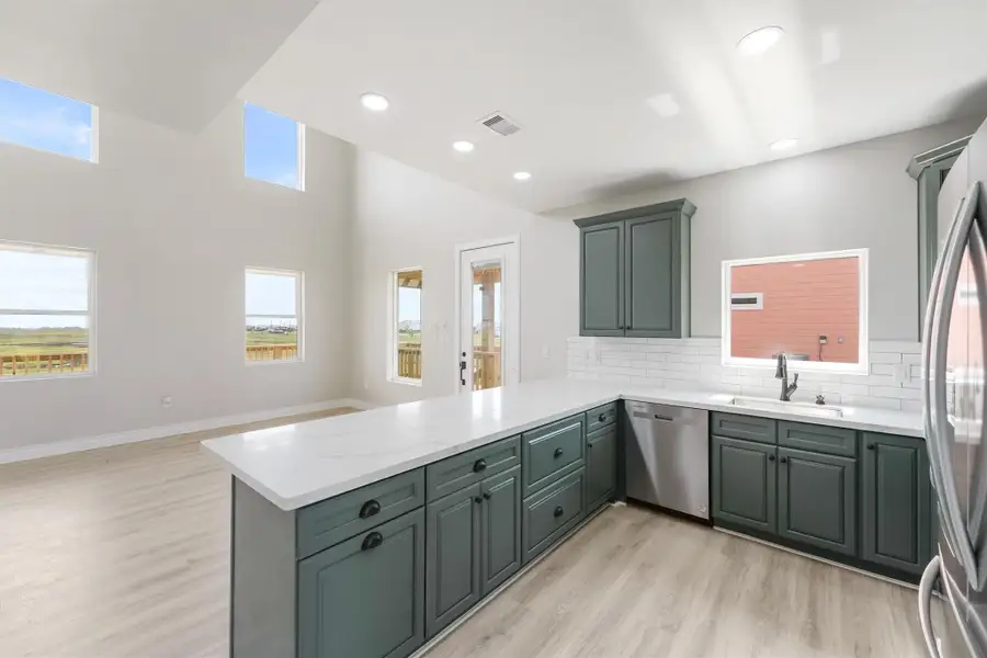 A modern kitchen with sleek, dark cabinetry, white countertops, and stainless steel appliances. It opens up to a spacious area with high ceilings and large windows, offering plenty of natural light and scenic views. A modern kitchen with sleek, dark cabinetry, white countertops, and stainless steel appliances. It opens up to a spacious area with high ceilings and large windows, offering plenty of natural light and scenic views.