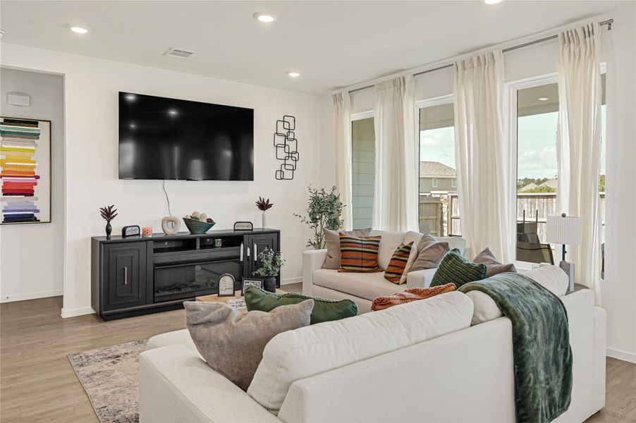 Bright and inviting living room featuring a spacious sectional sofa, large windows with sheer curtains, and a sleek entertainment center under a mounted TV. Bright and inviting living room featuring a spacious sectional sofa, large windows with sheer curtains, and a sleek entertainment center under a mounted TV.
