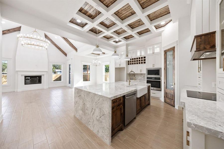 Kitchen featuring beamed ceiling, white cabinets, light stone counters, high vaulted ceiling, and a center island with sink