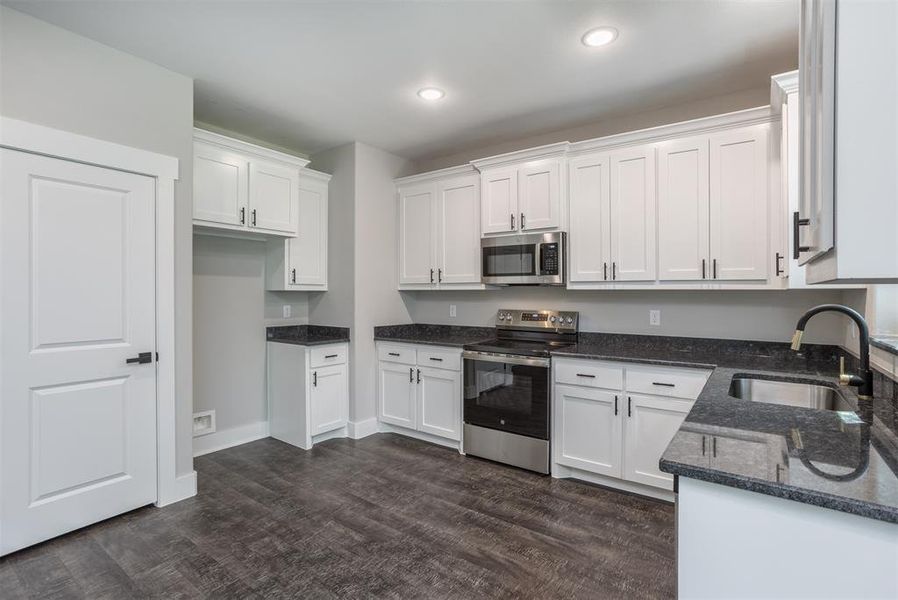 Kitchen with dark stone countertops, appliances with stainless steel finishes, white cabinets, dark wood-style flooring, and recessed lighting Kitchen with dark stone countertops, appliances with stainless steel finishes, white cabinets, dark wood-style flooring, and recessed lighting