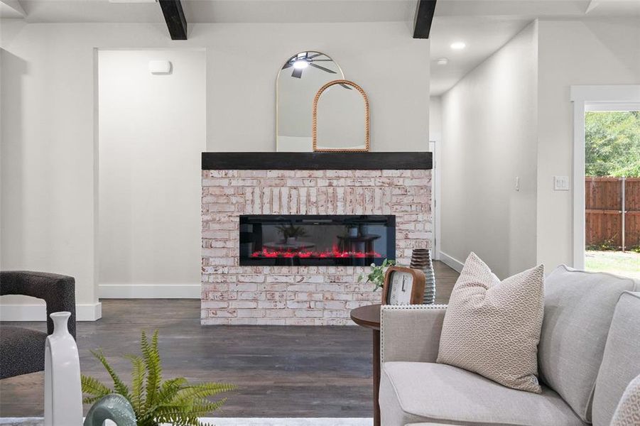 Living area featuring a white-washed brick fireplace with a dark wood mantle, dark wood-finish flooring, and white baseboards Living area featuring a white-washed brick fireplace with a dark wood mantle, dark wood-finish flooring, and white baseboards