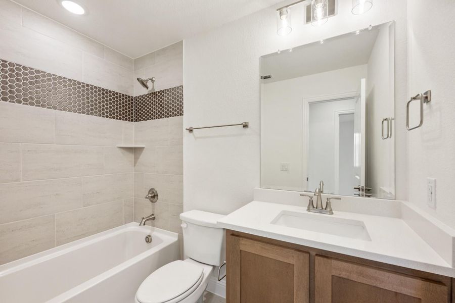 Bathroom with tiled tub surround, wood vanity, white countertop, and large mirror with pendant lights
