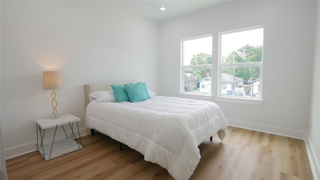 A bright, minimalist bedroom with wood flooring, featuring a cozy bed with white and teal accents. Two large windows provide ample natural light, and a modern lamp sits on a sleek side table. A bright, minimalist bedroom with wood flooring, featuring a cozy bed with white and teal accents. Two large windows provide ample natural light, and a modern lamp sits on a sleek side table.