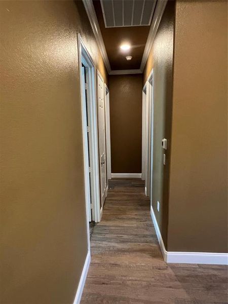Corridor with ornamental molding, dark wood-type flooring, and a textured wall Corridor with ornamental molding, dark wood-type flooring, and a textured wall