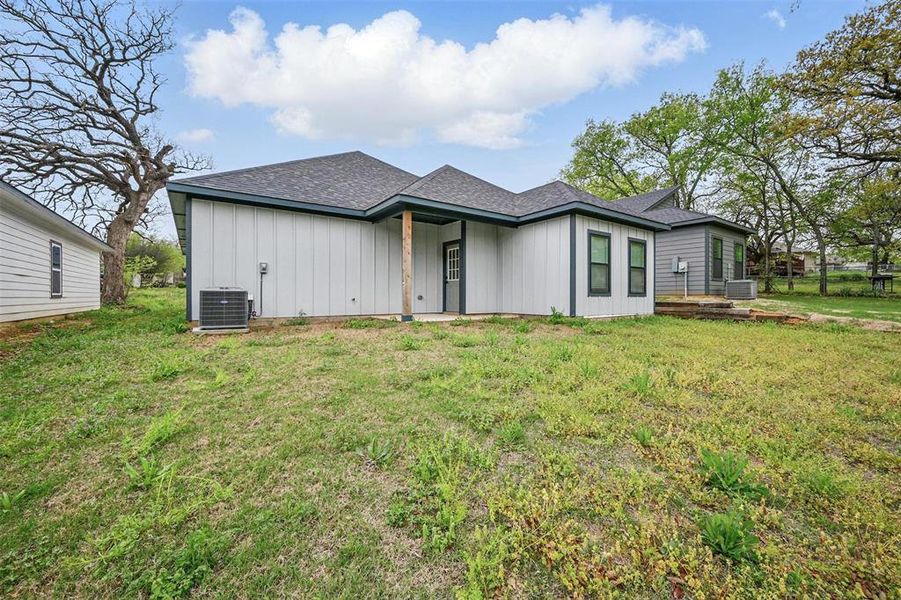 View of front of property with a front yard, cooling unit, board and batten siding, and roof with shingles