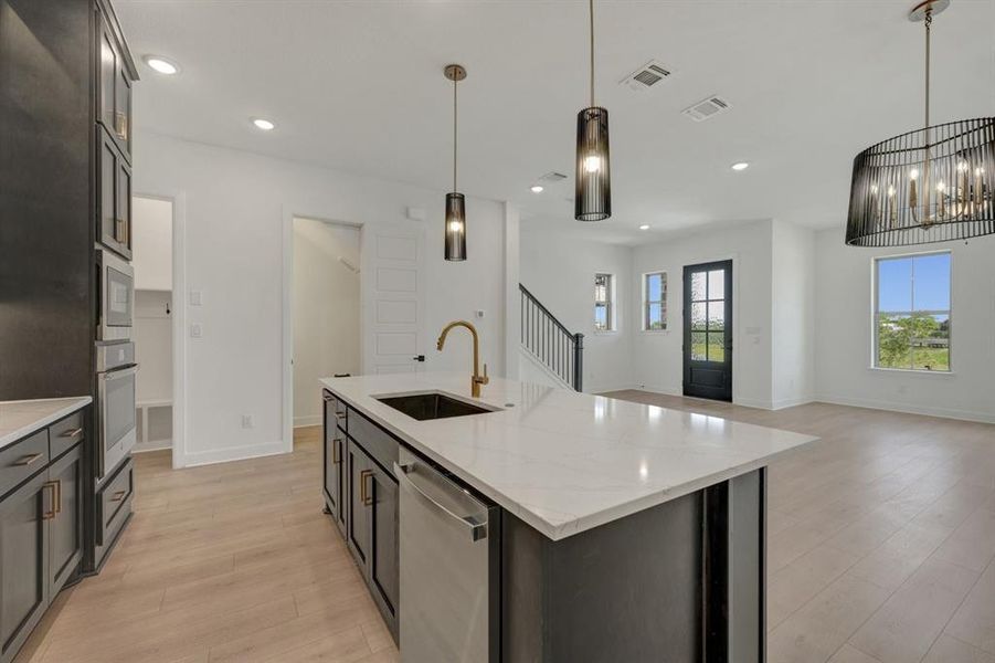 Contemporary kitchen featuring a large island with white stone countertop, integrated sink, and bronze-finish faucet Contemporary kitchen featuring a large island with white stone countertop, integrated sink, and bronze-finish faucet