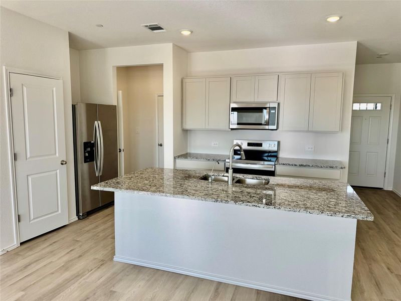 Kitchen with stainless steel appliances, light wood-style floors, light stone counters, an island with sink, and white cabinetry