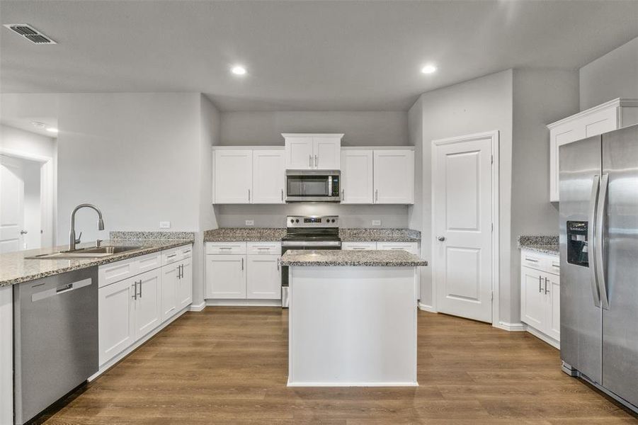 Kitchen with hardwood / wood-style floors, appliances with stainless steel finishes, white cabinetry, and sink