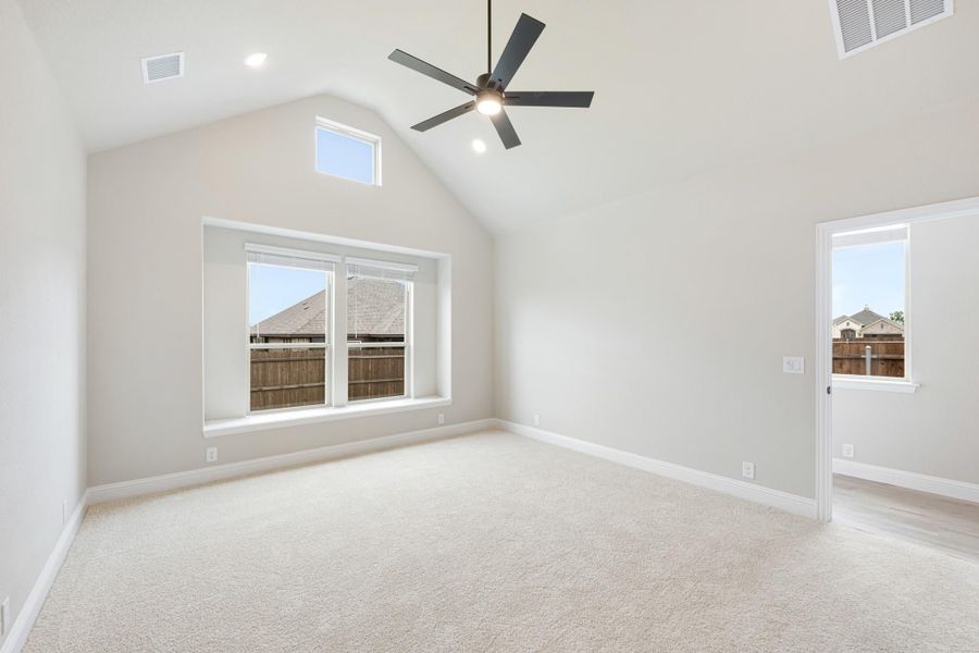 Empty bedroom with vaulted ceiling, ceiling fan, carpet flooring, and large windows