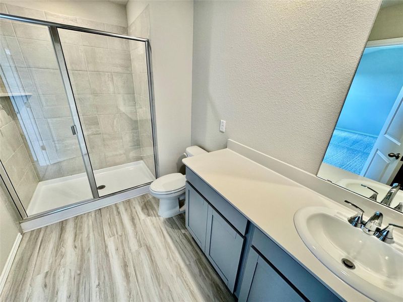 Bathroom with vanity, wood finished floors, a textured wall, and a stall shower Bathroom with vanity, wood finished floors, a textured wall, and a stall shower