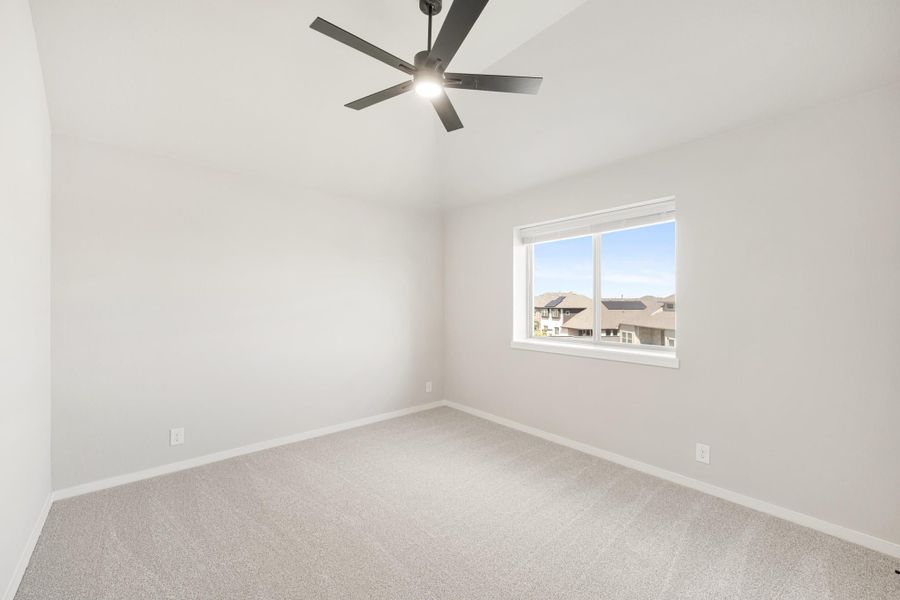 Empty bedroom with light carpet, vaulted ceiling, black ceiling fan, and single window with neighborhood view
