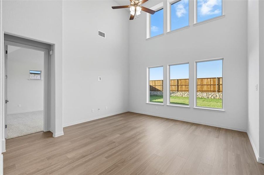 Unfurnished living room featuring a towering ceiling, light wood finished floors, and ceiling fan Unfurnished living room featuring a towering ceiling, light wood finished floors, and ceiling fan