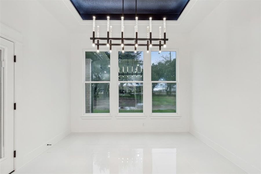 Unfurnished dining area featuring a chandelier, tile patterned flooring, and a tray ceiling