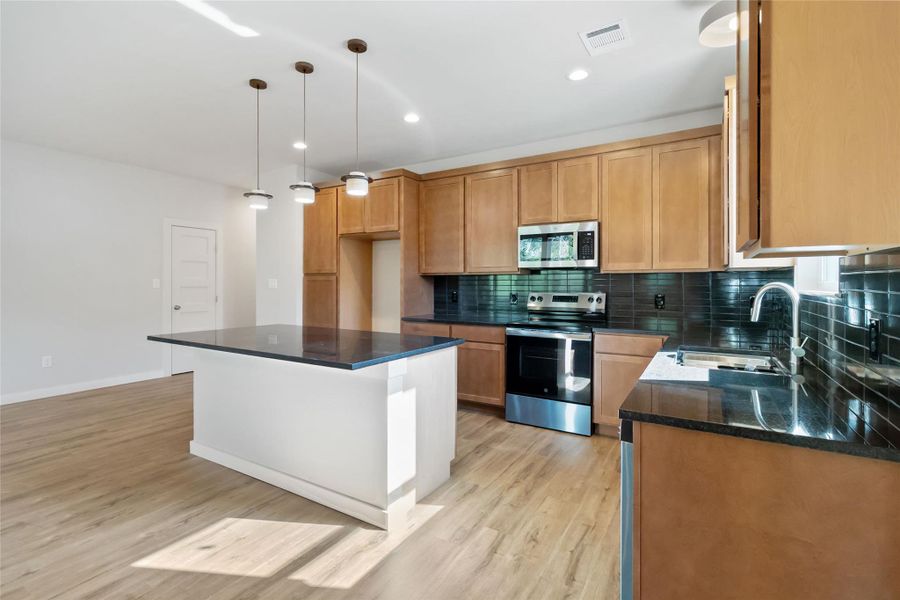 Kitchen featuring stainless steel appliances, tasteful backsplash, light wood-type flooring, recessed lighting, and hanging light fixtures