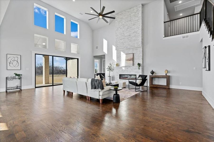 Living room featuring a fireplace, dark hardwood / wood-style floors, ceiling fan, and a high ceiling