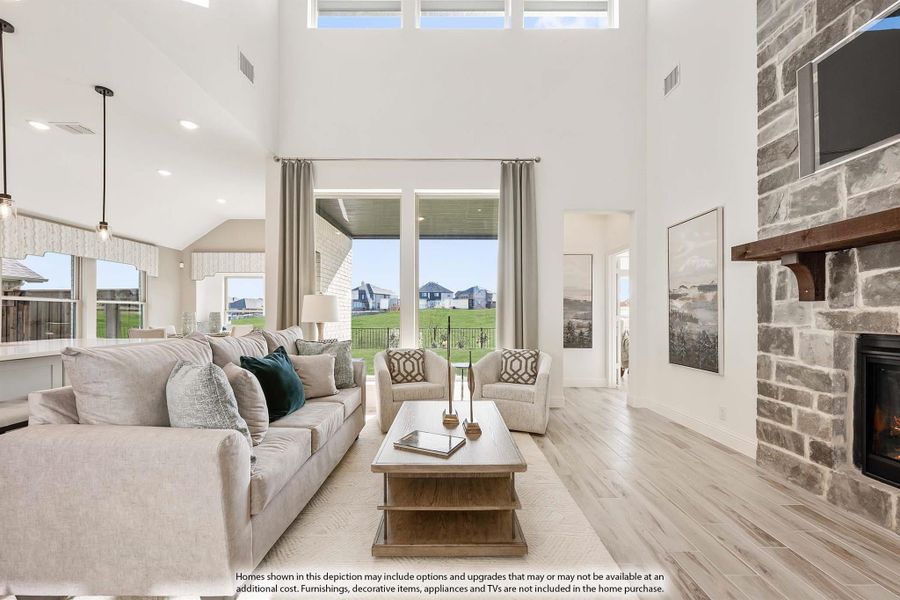 Open living room with two-story ceilings, stone fireplace, hardwood floors, and large windows with backyard views Open living room with two-story ceilings, stone fireplace, hardwood floors, and large windows with backyard views