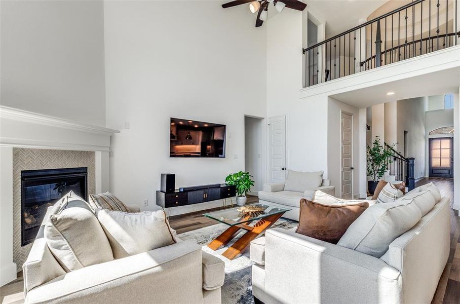 Living room with wood finished floors, a fireplace, a ceiling fan, and a high ceiling