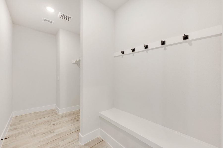 Mudroom with built-in bench, dark metal coat hooks, and light wood-look flooring Mudroom with built-in bench, dark metal coat hooks, and light wood-look flooring