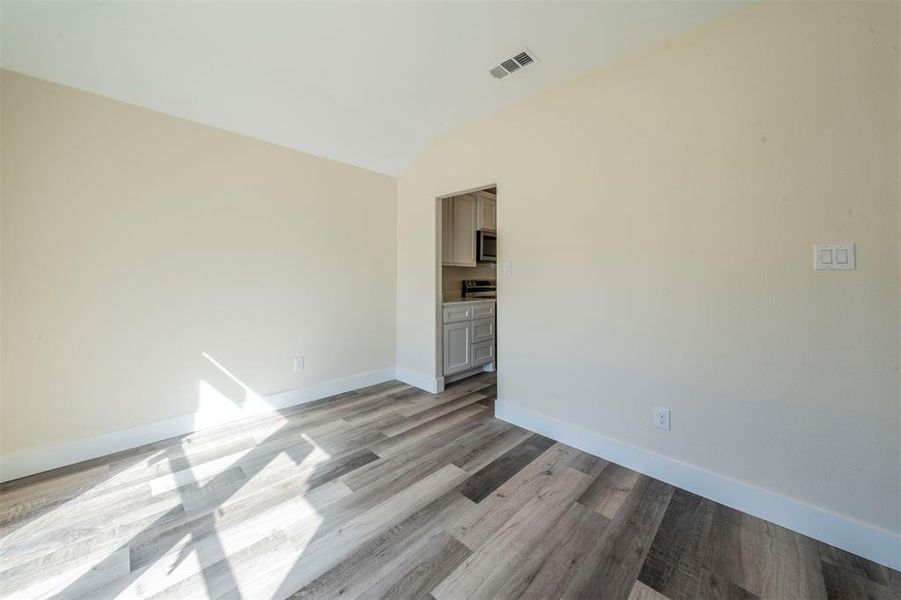 Empty room featuring visible vents, vaulted ceiling, light wood finished floors, and baseboards