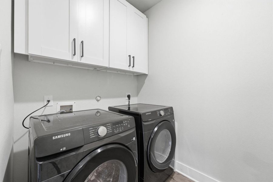 Dedicated laundry room featuring Samsung front-load washer and dryer, upper cabinetry for storage, and a clean, modern design.