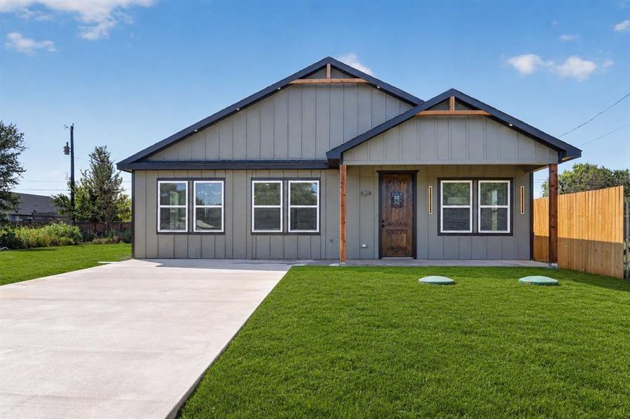 Contemporary-style home featuring board-and-batten siding in a neutral tone, a covered front porch with natural wood posts, a dark-stained wood entry door, a concrete driveway, and a manicured front lawn