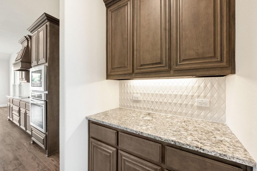 Kitchen with dark brown cabinets, granite countertops, patterned tile backsplash, and double wall ovens