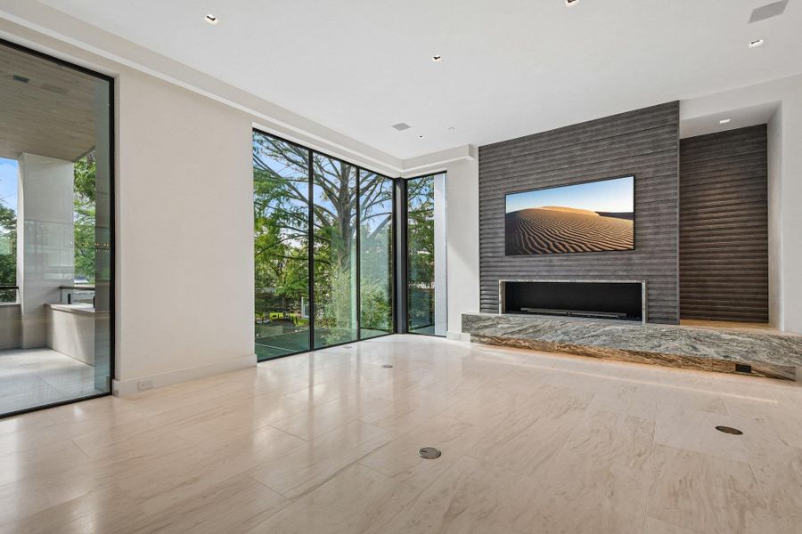Floor-to-ceiling windows frame verdant outdoor views alongside a sleek linear fireplace with stone hearth. Floor-to-ceiling windows frame verdant outdoor views alongside a sleek linear fireplace with stone hearth.