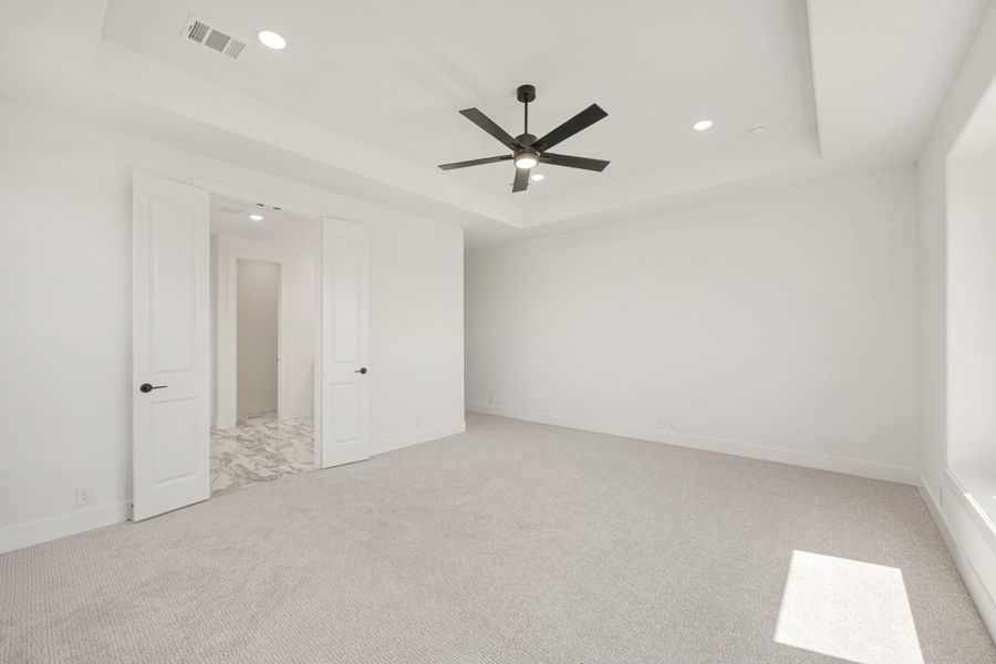 Empty bedroom with tray ceiling, black ceiling fan, carpet flooring, and open door to hallway