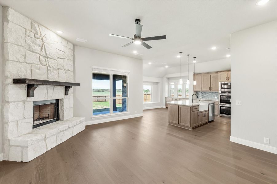 Open living area with white stone fireplace, hardwood floors, and kitchen island visible in background Open living area with white stone fireplace, hardwood floors, and kitchen island visible in background