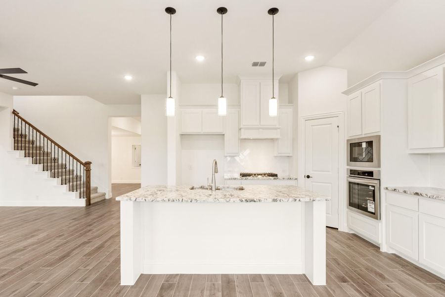 White kitchen with large island, granite countertops, pendant lights, and stainless steel double ovens