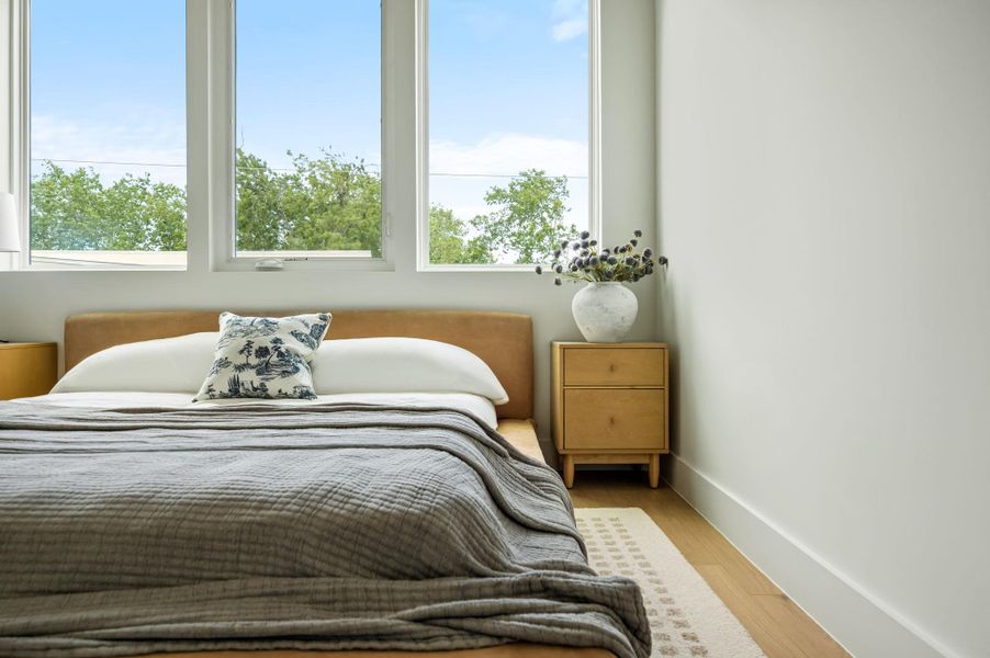 Natural light floods this inviting bedroom through tall windows, illuminating warm hardwood floors.