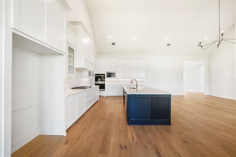 Kitchen with tasteful backsplash, white cabinetry, light wood-style flooring, a kitchen island with sink, and decorative light fixtures