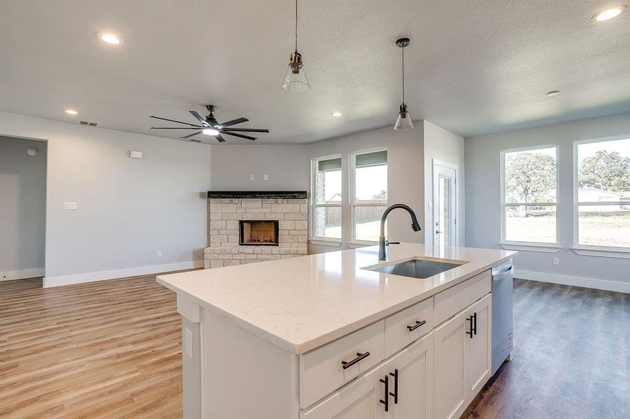 Kitchen featuring pendant lighting, a stone fireplace, white cabinetry, open floor plan, and recessed lighting