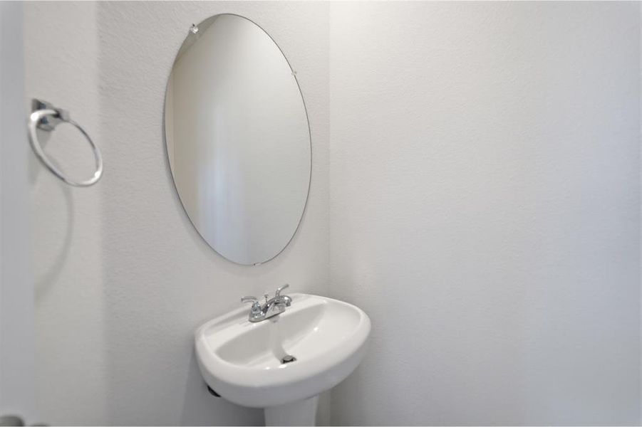 Pedestal sink with chrome-finish faucet and oval frameless mirror