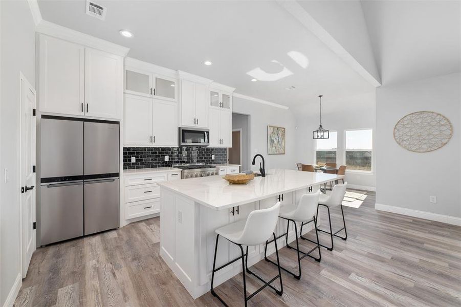 Kitchen with appliances with stainless steel finishes, white cabinetry, hanging light fixtures, a center island with sink, and a kitchen bar