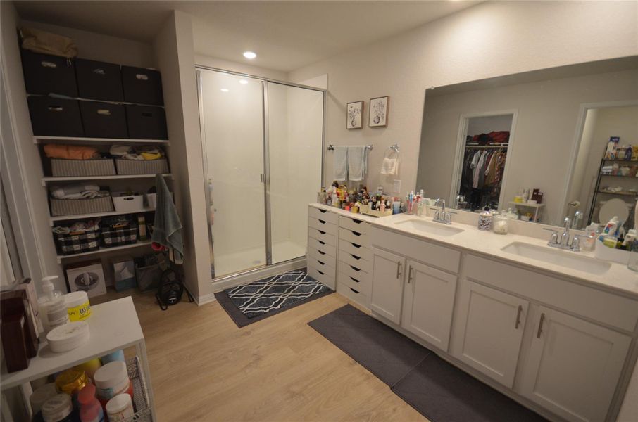 Full bathroom featuring wood finished floors, a stall shower, double vanity, a walk in closet, and recessed lighting Full bathroom featuring wood finished floors, a stall shower, double vanity, a walk in closet, and recessed lighting