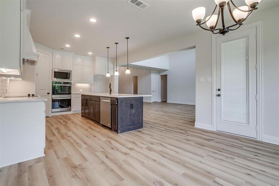 Kitchen with stainless steel appliances, decorative backsplash, white cabinets, a center island with sink, and light hardwood / wood-style floors