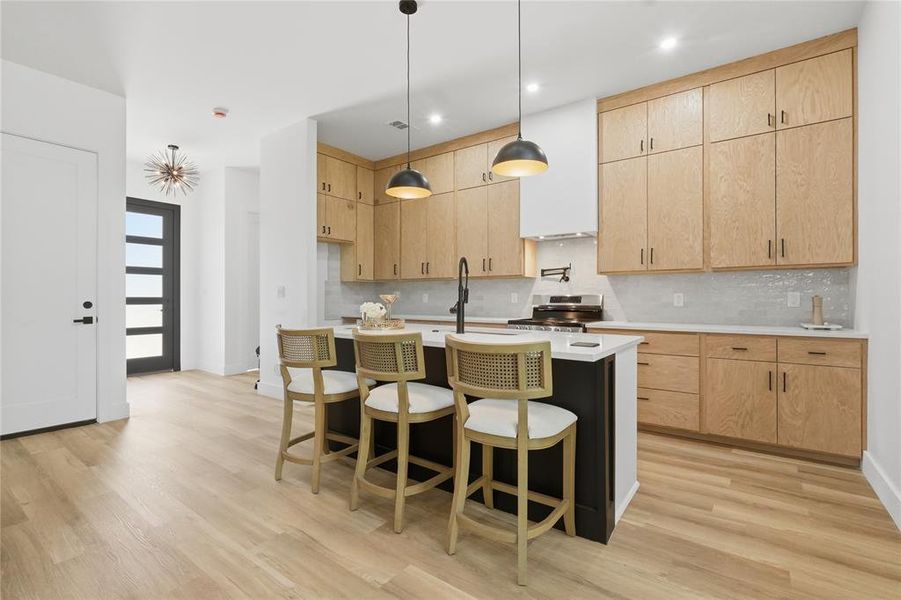 Modern kitchen featuring a central island with seating, light wood-finish flooring, light wood cabinetry, white countertops, and a full-height tile backsplash