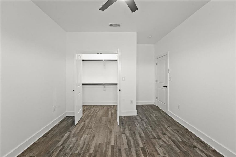 Unfurnished bedroom featuring a walk in closet, dark wood-type flooring, a closet, and ceiling fan