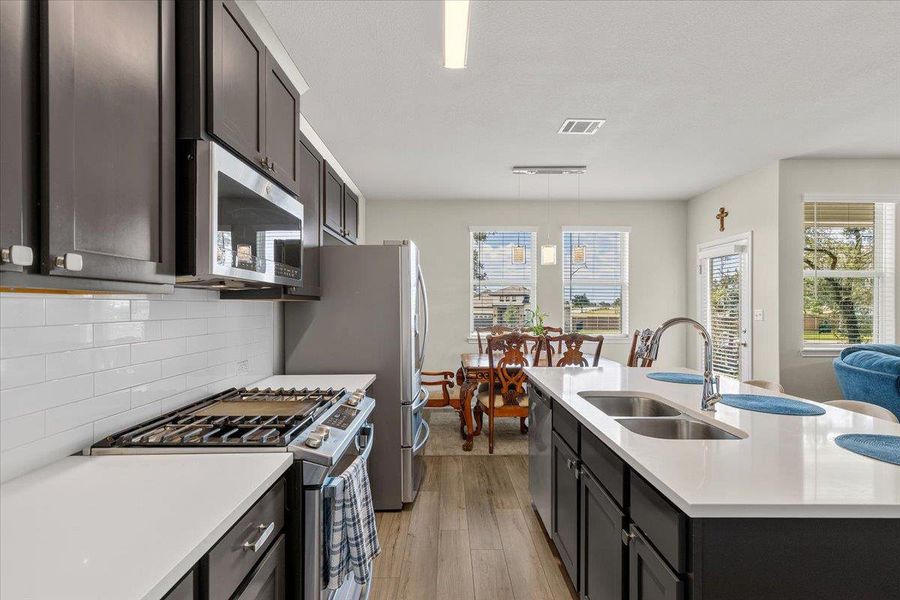 Dark cabinetry and quartz countertops frame a modern kitchen with an adjacent dining area.