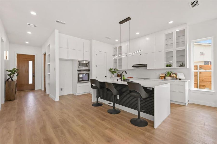 Kitchen featuring modern cabinets, white cabinets, a kitchen bar, glass insert cabinets, and appliances with stainless steel finishes Kitchen featuring modern cabinets, white cabinets, a kitchen bar, glass insert cabinets, and appliances with stainless steel finishes